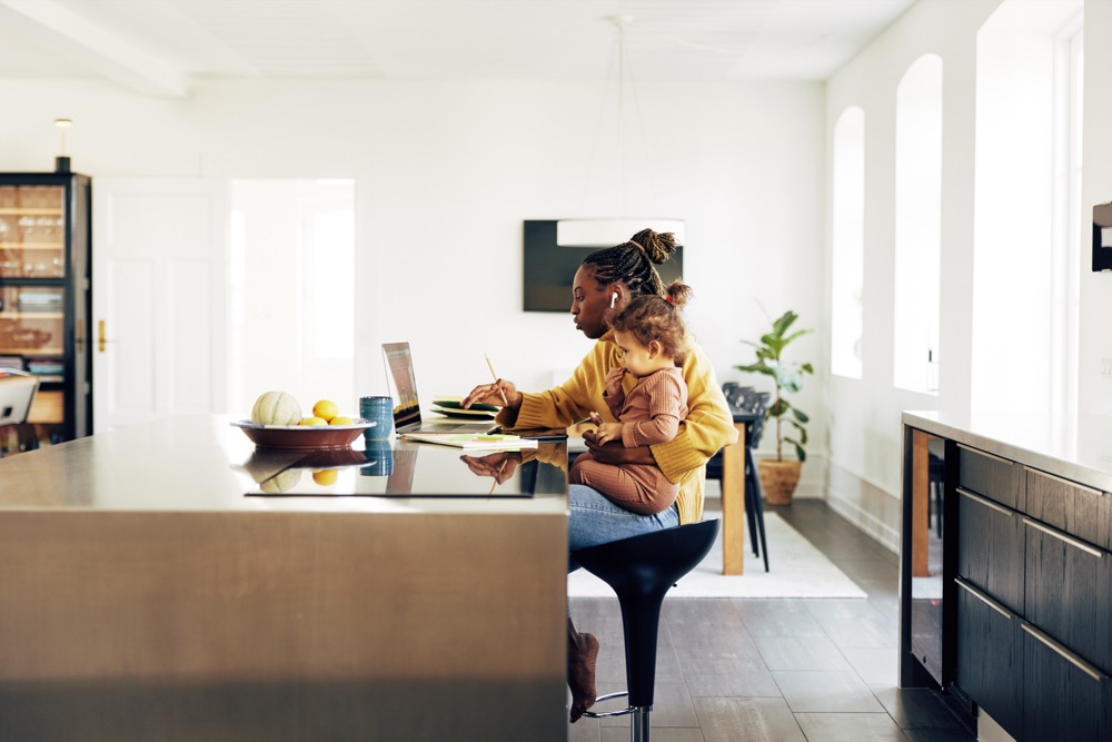 A founder working at her kitchen counter while holding her toddler.